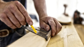 Carpenter using carpenter's square and pencil to mark molding to be cut.
